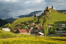 Scenic Landscape Of Early Summer Morning In The Depths Of The Caucasus Mountains. Sun Just Came Out And Illuminates Ancient Ruins Of Tushetian Towers. Below The Ruins Is The Village Upper Omalo.
