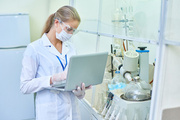 Wall Mural - Portrait of blonde female scientist using laptop while working in medical laboratory doing internet research, copy space