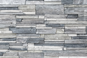 A gray wall of narrow uneven stones. Horizontal pattern.