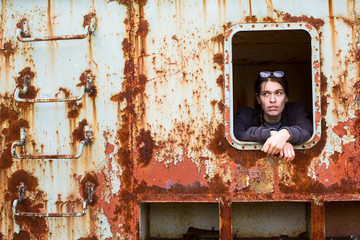 Portrait of a young woman in the window of an abandoned iron rusty object.