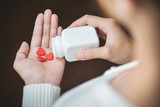 Fototapeta Na sufit - Female holding a white pill bottle and red pills in heart shape.