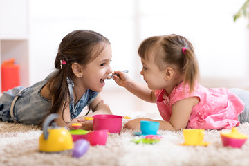cute little children playing with kitchenware while lying on floor at home