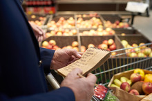 Close up of senior man holding shopping list while grocery shopping in supermarket, fruits and vegetables in background, copy space