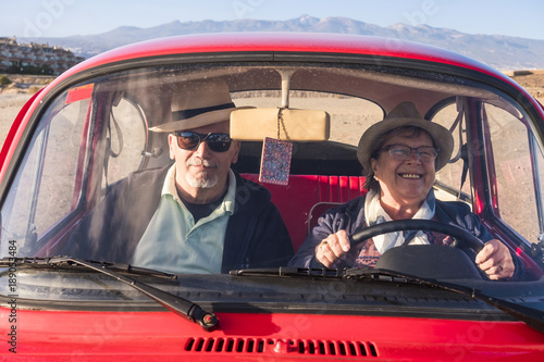 Photographie elderly couple with hats inside old red car