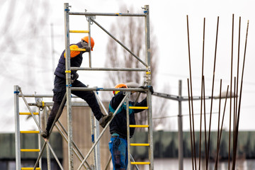 Two workers  build metal scaffolding on construction site