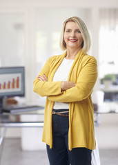 Wall Mural - Smiling businesswoman standing at the office. Portrait of an arms crossed smiling financial business woman standing at the office.