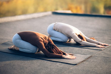 Two young women doing yoga asana child's pose on the roof outdoor