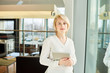 © Seventyfour - Waist-up portrait of confident young entrepreneur with digital tablet in hands looking at camera while standing at spacious office lobby with panoramic windows
