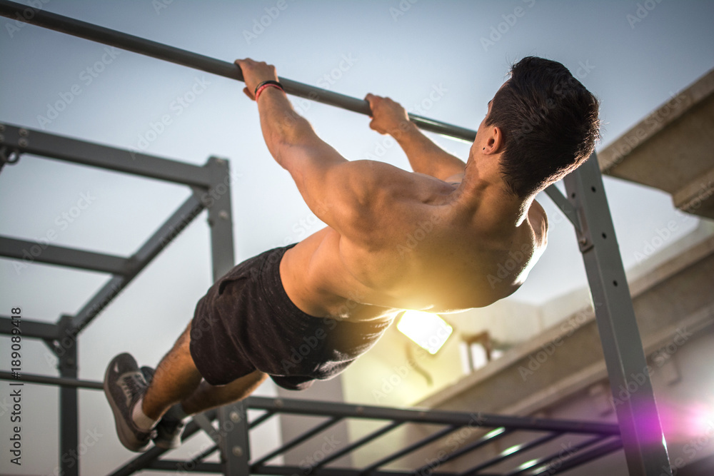 Back view of handsome shirtless man exercising on horizontal bar outdoors. Calisthenics workout. - obrazy, fototapety, plakaty 