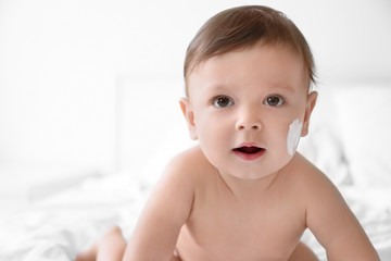 Wall Mural - Cute baby with body cream on cheek against light background