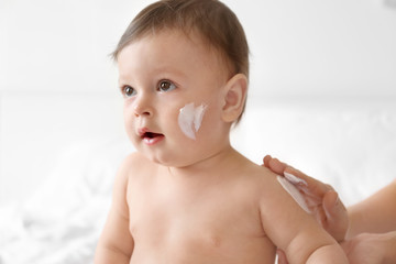 woman applying body cream on her baby against light background