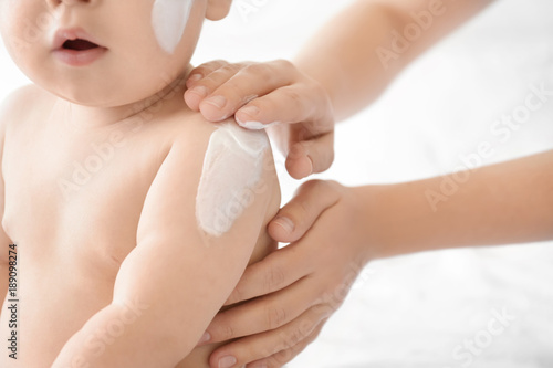Fotografía Woman applying body cream on her baby against light background