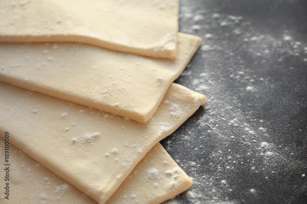 Raw flaky dough with flour on table
