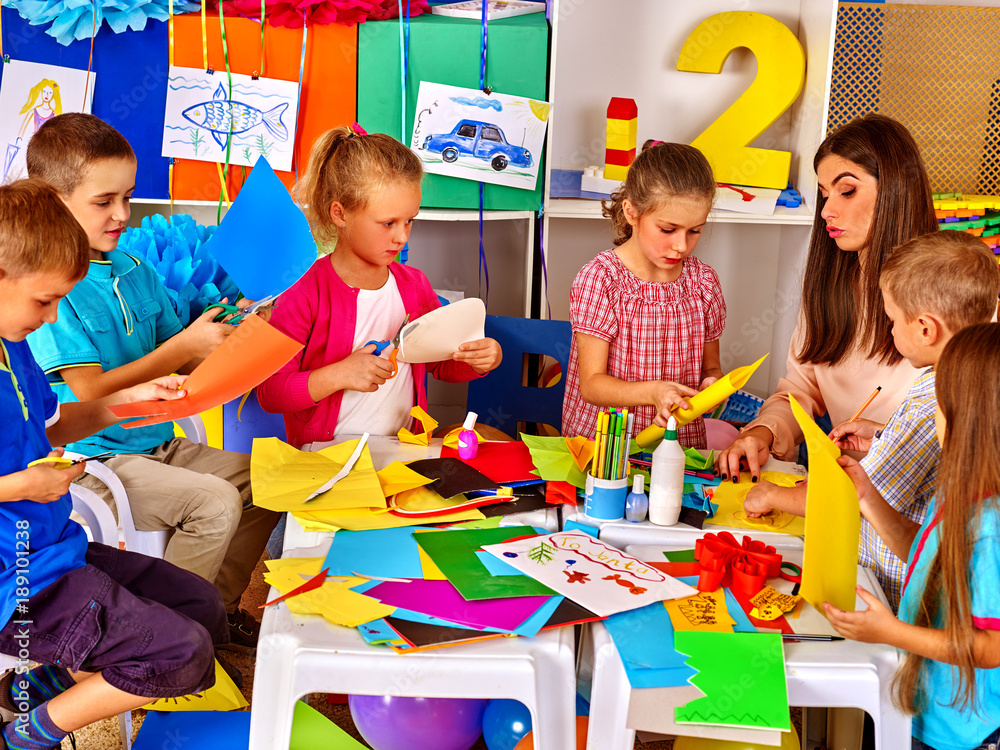Children and colored paper. Making something on table in primary school ...