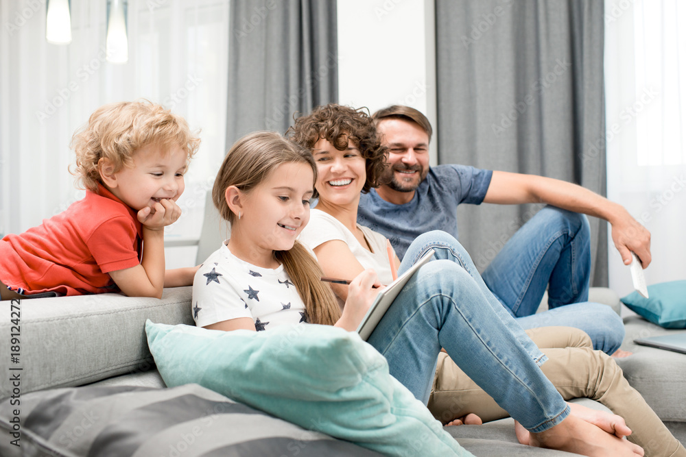 Joyful family of four gathered together in cozy living room and enjoying each others company, pretty little girl drawing picture with pencil - obrazy, fototapety, plakaty 