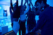 © Seventyfour - Group of modern young people dancing listening to DJ playing music at private house party, focus on beautiful girls lit by blue light