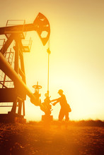 Oil Worker Is Checking The Oil Pump On The Sunset Background.