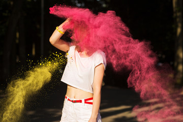 Slim young woman having fun in a cloud of yellow and pink dry paint at Holi festival