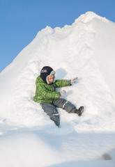 a boy in a green jacket is riding on a hill of snow