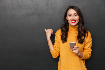 Wall Mural - Smiling brunette woman in sweater holding smartphone