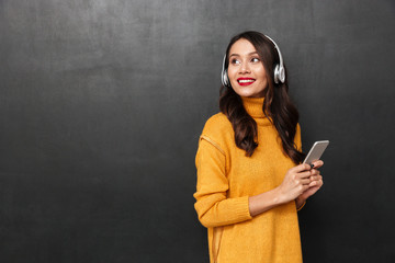 Poster - Smiling woman in sweater and headphones listening music by smartphone