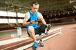 © Seventyfour - Full length portrait of young amputee athlete taking break from practice relaxing sitting on bench eating sandwich and using smartphone