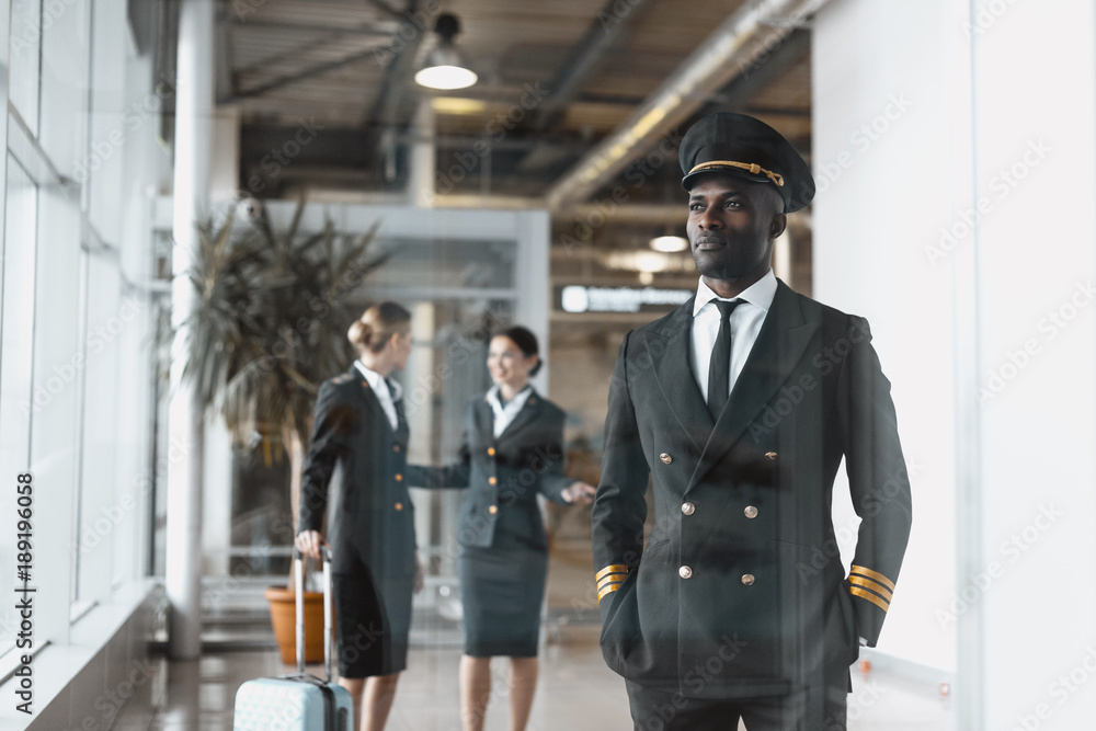 thoughtful young pilot in airport with stewardesses before flight - obrazy, fototapety, plakaty 