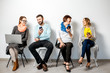 © rh2010 - People in colorful casual clothes using gadgets sitting in a row on the white wall background