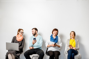 People in colorful casual clothes using gadgets sitting in a row on the white wall background