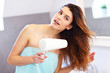 © Kalim - Young woman using hair dryer in bathroom in the morning