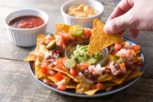 People Eating Mexican Nachos With Beef, Guacamole, Cheese Sauce, Peppers, Tomato And Onion In Plate On Wooden Table