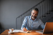 © LUMINA IMAGES - Handsome Caucasian smiling businessman using his laptop and writing in his notebook at cafe.