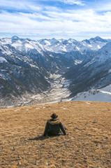 young man sitting in the sun surrounded by snowy mountains and looking down.