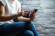 © Sebastian - Woman sitting at the wall and browsing the phone. Online shopping, web browsing, email, private messages. Woman finger clicks on phone to browse content, mobility concept and online shopping.
