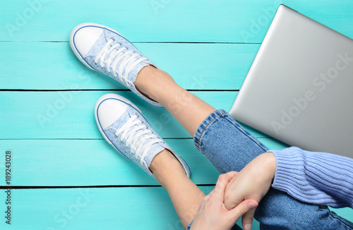 Female Legs In Jeans And Sneakers Laptop On A Turquoise Wooden