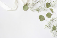 Styled Stock Photo. Feminine Wedding Desktop Mockup With Baby's Breath Gypsophila Flowers, Dry Green Eucalyptus Leaves, Satin Ribbon And White Background. Empty Space. Top View. Picture For Blog.