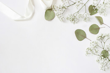 Styled stock photo. Feminine wedding desktop mockup with baby's breath Gypsophila flowers, dry green eucalyptus leaves, satin ribbon and white background. Empty space. Top view. Picture for blog.