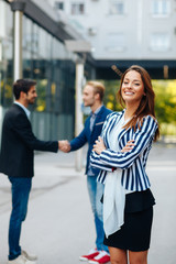 Wall Mural - Young businesswoman posing in front of two man shaking hands