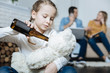 © zinkevych - Beverage. Unhappy fair-haired little girl holding a bottle of beer and giving it to her teddy bear while her parents working on their laptops