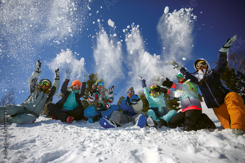 Fototapeta na szkło Grupa przyjaciół narciarzy i snowboardzistów bawi się rzucając śniegiem na szczyt góry.