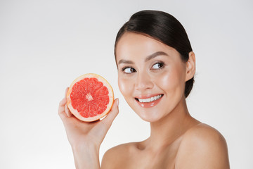 Canvas Print - Close up image of glad woman with healthy fresh skin holding juicy grapefruit and looking aside with smile, isolated over white background