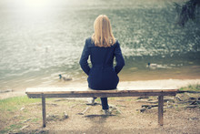 Model Woman Sitting On A Wooden Bench Near The Water. Rear View.