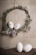 Easter Still life with decorative eggs in pastel colours, rope, ribbon and button with flower wreath on the wooden background