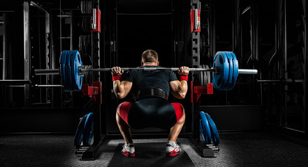 Professional athlete sits with a barbell on his shoulders and prepares to stand with her.