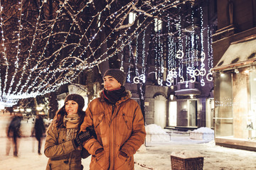 Young couple walking in winter city center under holiday illumination