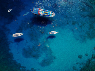 Aerial shot of beautiful blue lagoon at hot summer day with sailing boat. Top view of people are swimming around the boat.