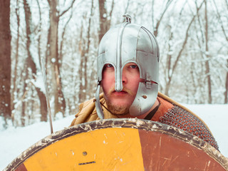 Medieval Irish warrior in chain mail and helmet holds a shield in the winter forest