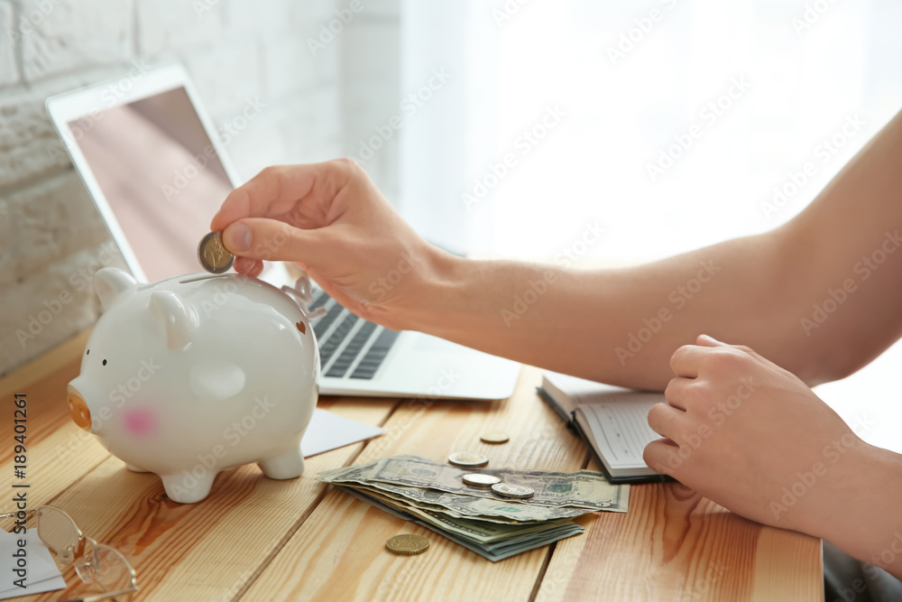Young man putting coin into piggy bank, closeup