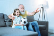 © zinkevych - Transmitting knowledge. Careful senior gentleman embracing his adorable granddaughter and pointing toward a TV screen while both sitting on a sofa and talking about football.