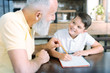 © zinkevych - Education is the key to success. Selective focus on hands of a senior man looking at his grandson and telling him something while both doing homework at a table.